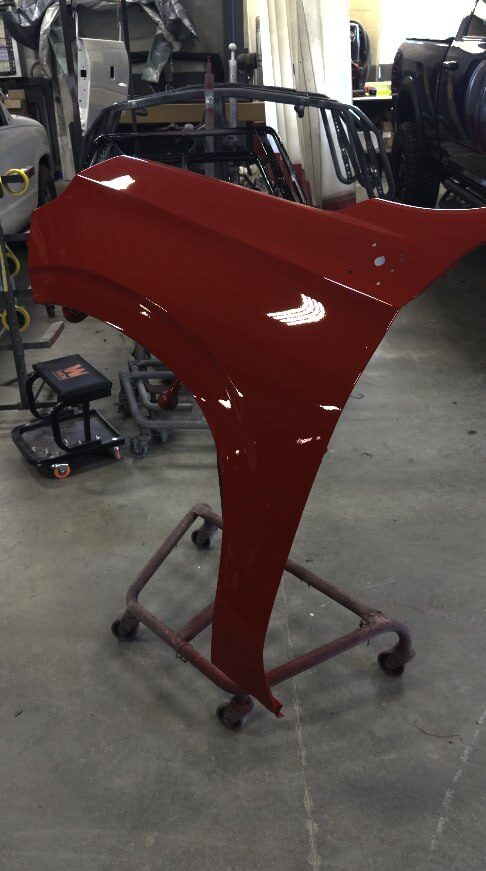 Freshly painted glossy red fender on a wheeled paint stand on the shop floor