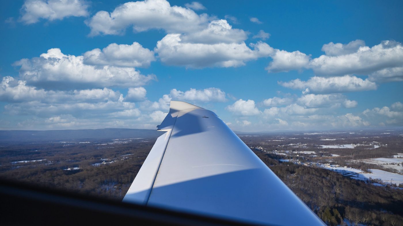 Over-wing view in flight above snow-covered fields with a ridge on the horizon