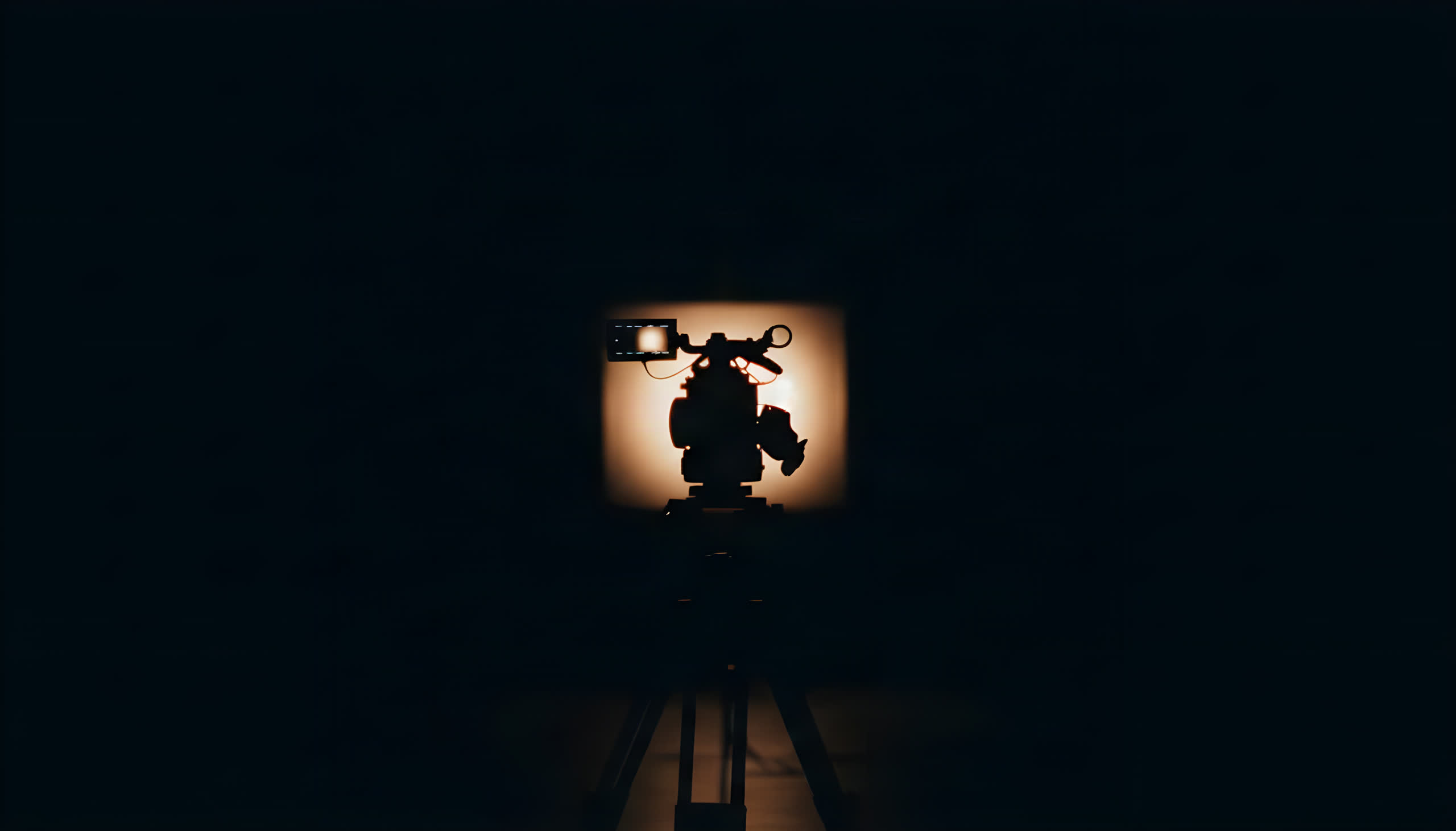 Silhouette of a video camera on a tripod, backlit in a dark studio